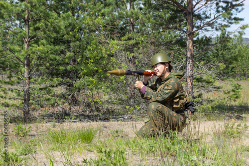 Fully armed asian soldier with bazooka takes aim for a shot in the summer forest, active military game airsoft.
