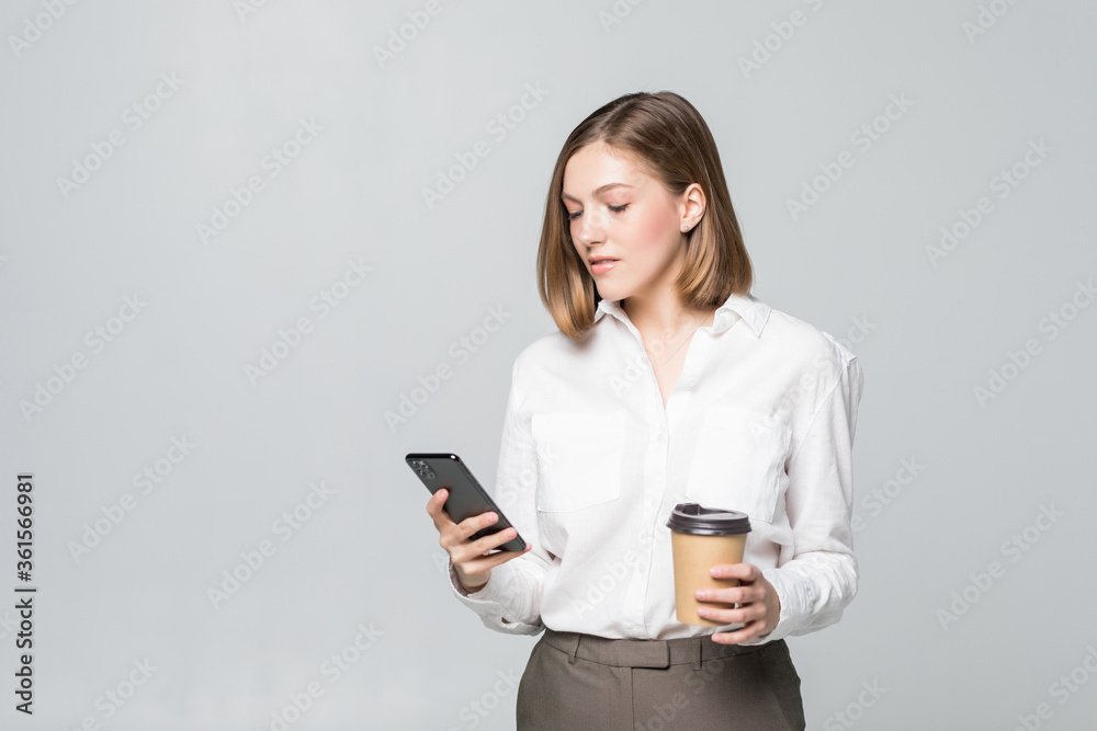 Portrait of a satisfied young business woman using mobile phone while holding cup of coffee to go over white background Portrait of a satisfied young business woman using mobile phone while holding cup of coffee to go over white background