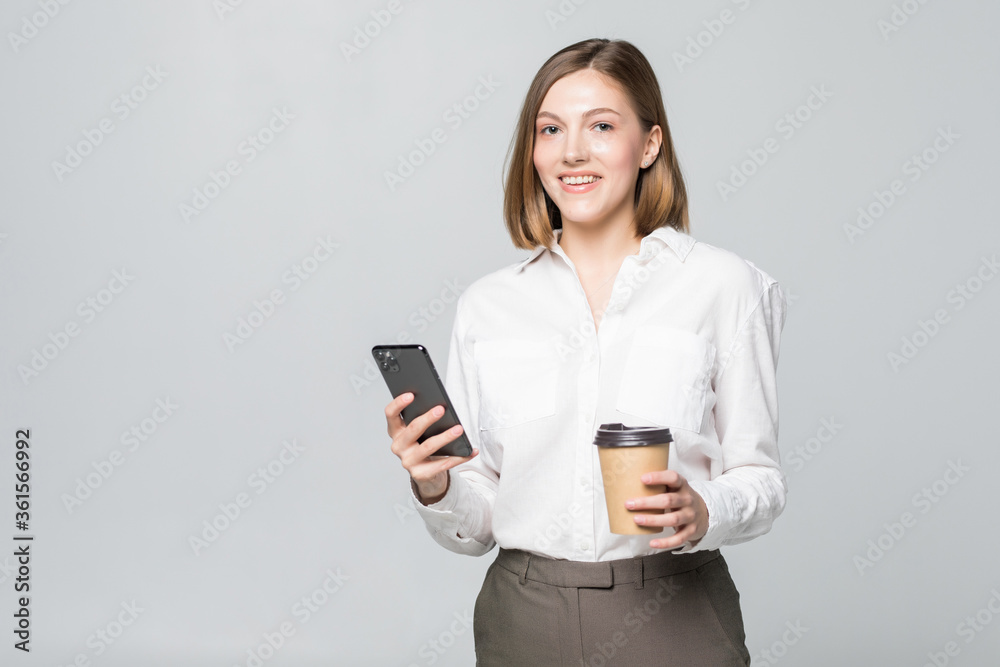 Portrait of a satisfied young business woman using mobile phone while holding cup of coffee to go over white background Portrait of a satisfied young business woman using mobile phone while holding cup of coffee to go over white background