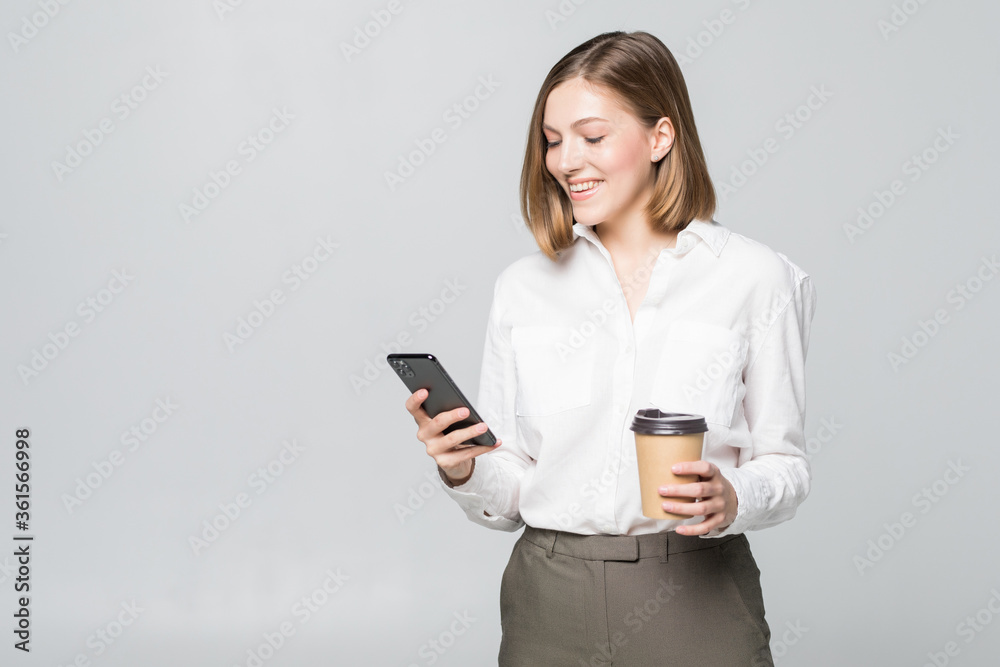 Portrait of a satisfied young business woman using mobile phone while holding cup of coffee to go over white background Portrait of a satisfied young business woman using mobile phone while holding cup of coffee to go over white background
