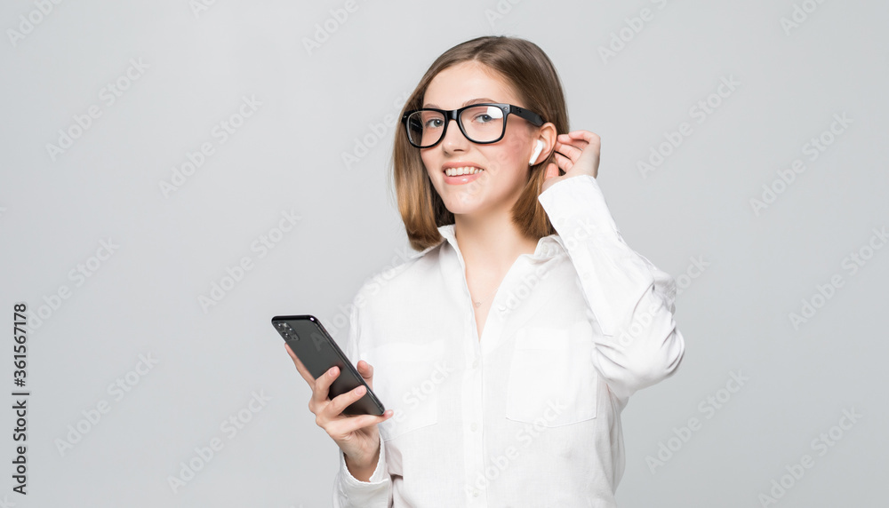 Young beautiful business woman talking via airpods wirrless headset holding phone isolated on white background Young beautiful business woman talking via airpods wirrless headset holding phone isolated on white background