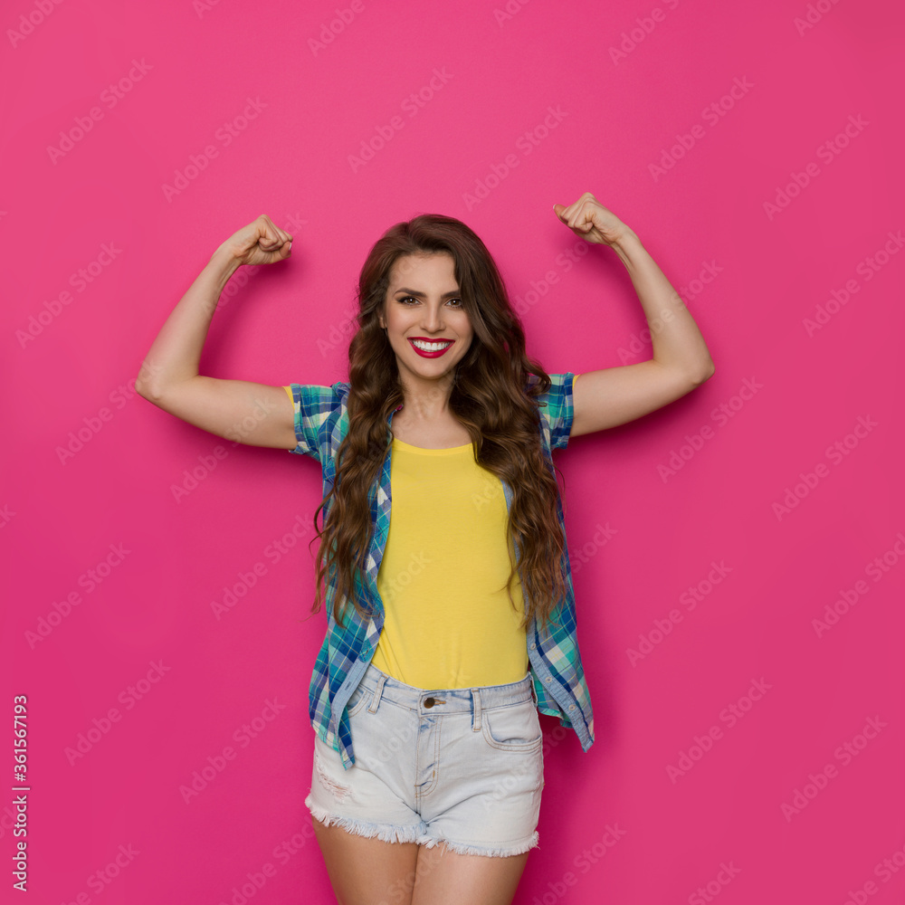 Strong Smiling Woman In Unbuttoned Lumberjack Shirt And Shorts Is Standing And Flexing Muscles Strong Smiling Woman In Unbuttoned Lumberjack Shirt And Shorts Is Standing And Flexing Muscles