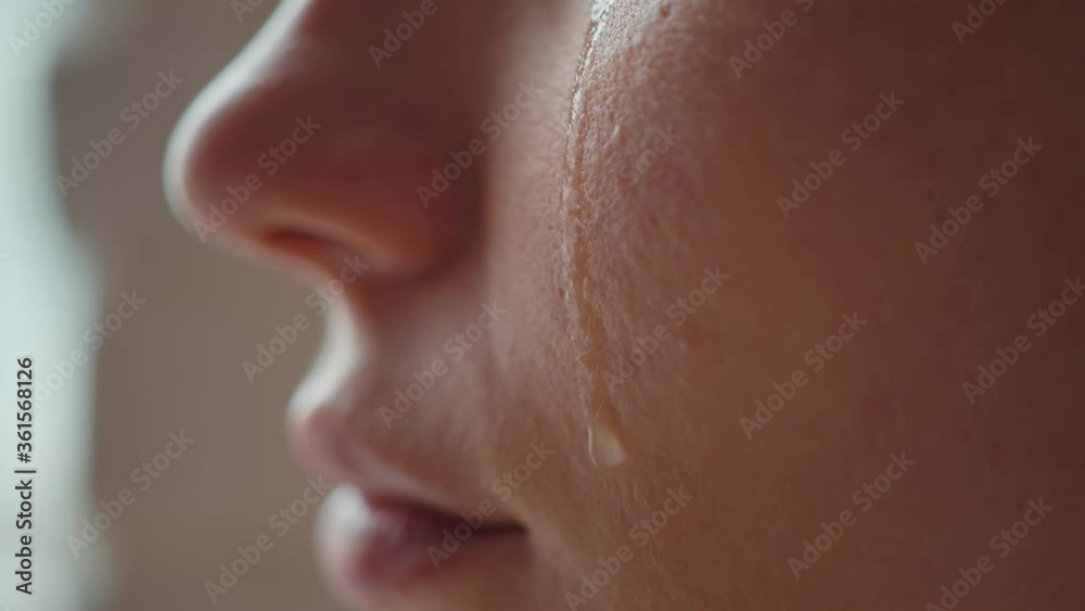 A macro tear runs down the cheek of a young girl, the girl smiles, out of desperation