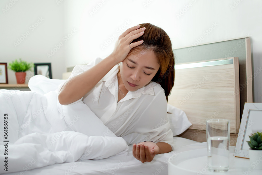 Asian woman is taking a headache medication on the bed. She has a headache and can't work. Asian woman is taking a headache medication on the bed. She has a headache and can't work.