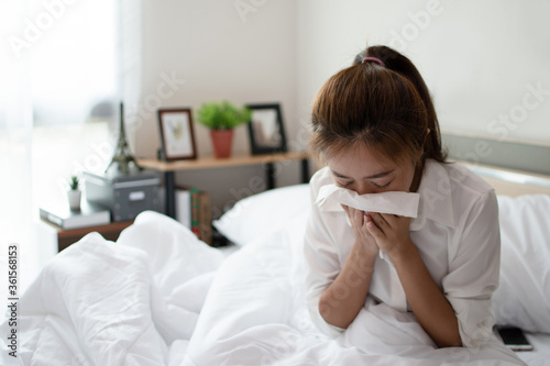 Young businesswoman is sick and coughs heavily on the bed in her room.