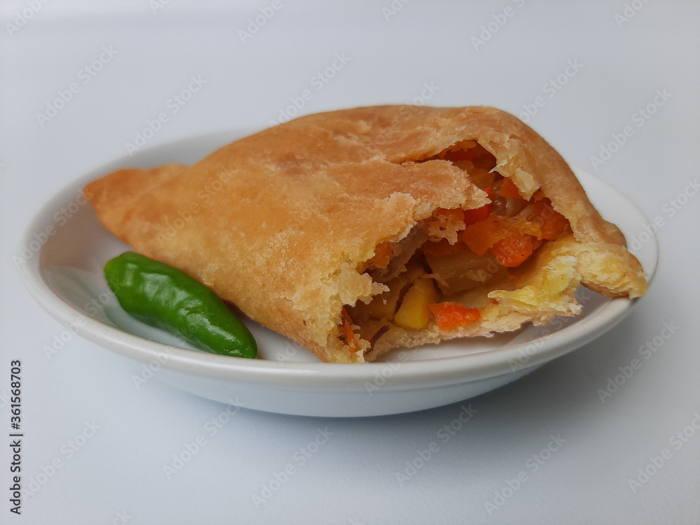Bitten pastel. Pastel is a popular snack from Indonesia. A pastry filled with chicken meat and mixed vegetable, then deep fried. Served with green chili. On white plate. Isolated in white background. Bitten pastel. Pastel is a popular snack from Indonesia. A pastry filled with chicken meat and mixed vegetable, then deep fried. Served with green chili. On white plate. Isolated in white background.