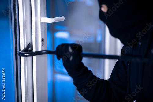 Fototapeta Robber in black balaclava cracking door with the crowbar