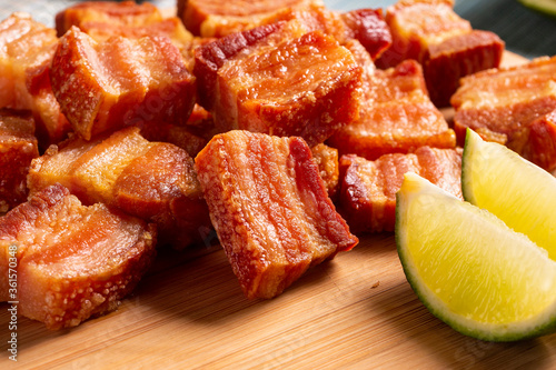 Deep fried crispy pork belly served with two half lemon on the table.