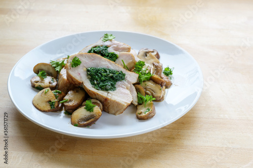 chicken breast fillet stuffed with spinach, served with mushrooms and parsley garnish on a light wooden table with copy space