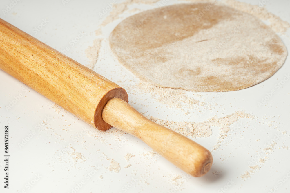The dough is rolled out in a circle on a white table near the rolling pin The dough is rolled out in a circle on a white table near the rolling pin