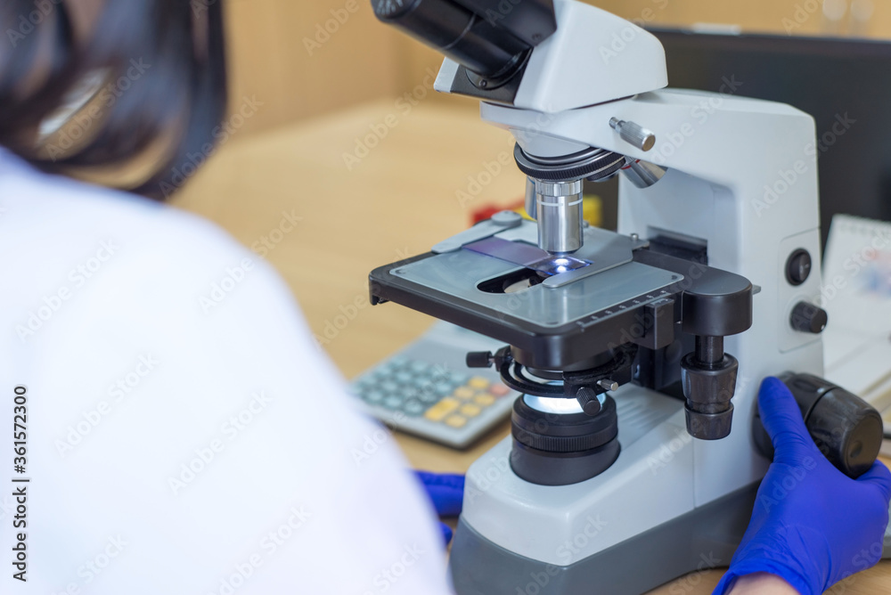 laboratory assistant is looking through a microscope. Close-up doctor laboratory assistant looking through a microscope, determining a blood test of a patient, red blood cells laboratory assistant is looking through a microscope. Close-up doctor laboratory assistant looking through a microscope, determining a blood test of a patient, red blood cells