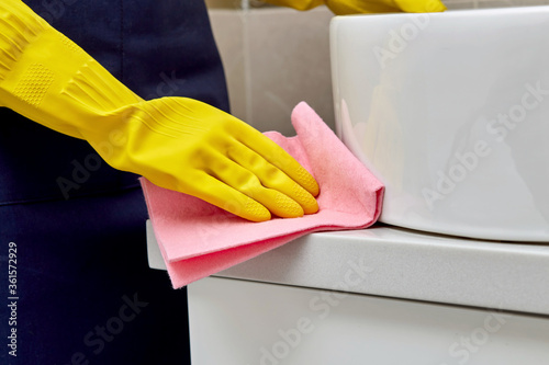 A man in rubber gloves with a napkin in his hands cleans a white wash basin.