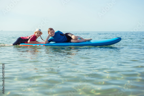 Two happy siblings teen children in neoprene suits having fun with sup board in Baltic sea