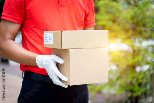 Close up of a delivery man holds parcels and boxes in front of the customer's house to deliver online shopping orders during the COVID-19 pandemic. The delivery person delivers parcel posts. © EduLife Photos