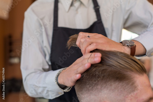 professional hands of hairdresser master styling hair for client barbershop, young guy. Hair care, collects hair in a ponytail, professional hair styling.