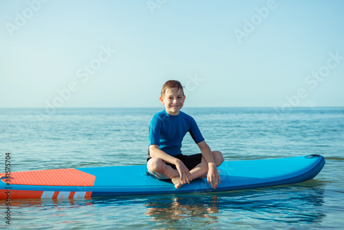Happy teen child boy having fun and making sport on sup board in Baltic sea
