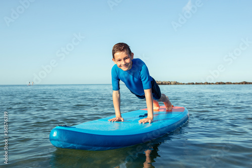 Happy teen child boy having fun and making sport on sup board in Baltic sea