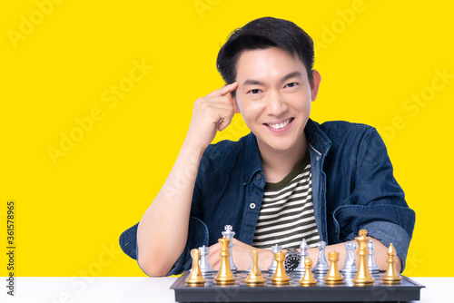 portrait asian glasses attrative male casual costime smile with cheerful and confident positive thinking to win chess board game competition victory isolate yellow background photo