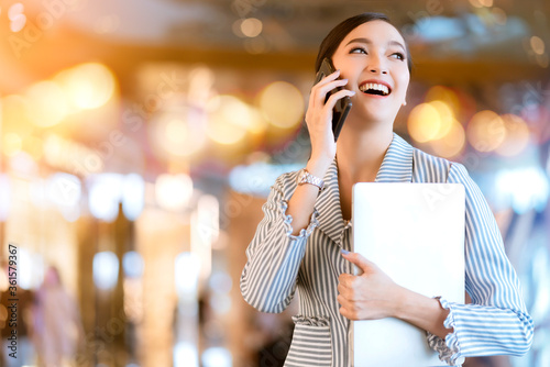 Asian female business owner hand communication with smartphone and laptop business technology with blur deaprtment store bokeh background photo