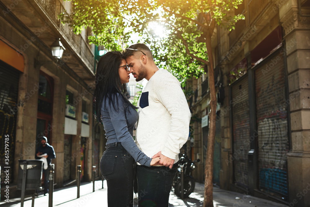 Fototapeta premium Good-looking woman and her attractive boyfriend stand very close to each other. The guy lovingly looks at his mate and holding her hand. She closed her eyes and dreaming about something pleasant.