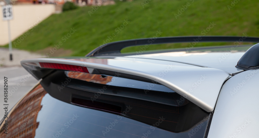 Close-up on the trunk lid of a gray car with a plastic spoiler over the rear window to improve the aerodynamics of the car body during tuning for racing. Close-up on the trunk lid of a gray car with a plastic spoiler over the rear window to improve the aerodynamics of the car body during tuning for racing.