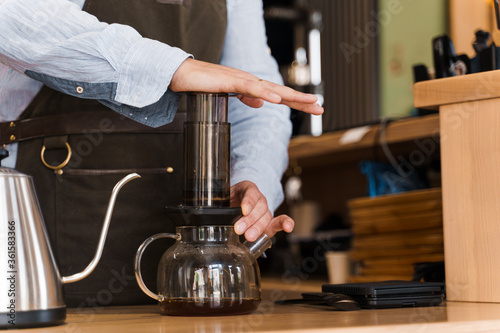 Aeropress coffee close-up: barista press to device and coffee drops pours trought aeropress to pot. Alternative scandinavian coffee brewing method.