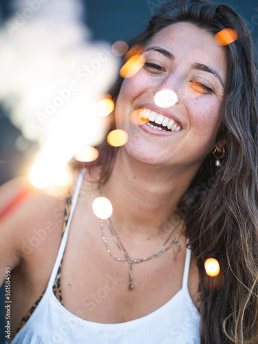 A young caucasian female smiling while holding a sparkler