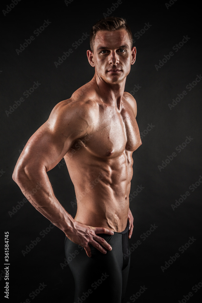 Fitness in gym, sport and healthy lifestyle concept. Handsome athletic man showing his trained body on black background. Bodybuilder male model training biceps muscles with dumbbell.