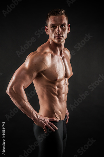 Fitness in gym, sport and healthy lifestyle concept. Handsome athletic man showing his trained body on black background. Bodybuilder male model training biceps muscles with dumbbell. © Maksim Toome