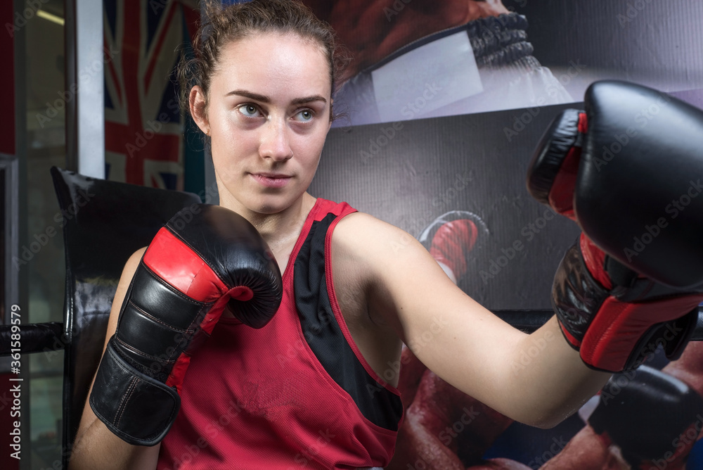 Portrait of a young girl, twenty years old, in sports uniform and boxing gloves, protected from bumps. In a boxing club. Ring, rope. Sportswoman in boxing training. Girls in martial arts