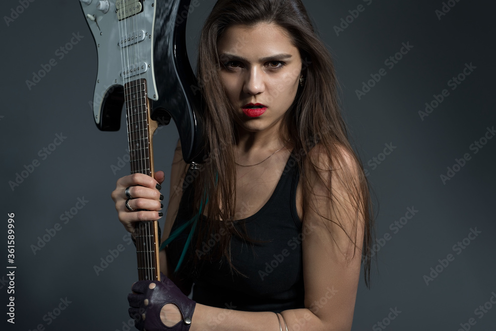 beautiful girl holding an electric guitar in her hands, looking at the camera. Studio portrait on a gray background