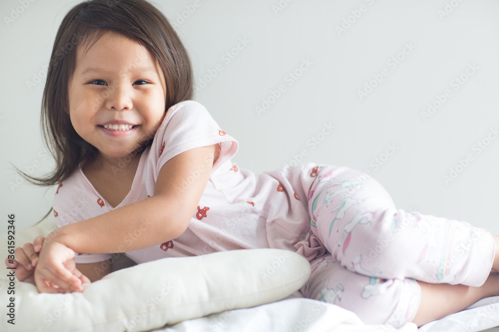Portrait of cute little asian girl posing and smiling to the camera while laying in bed wearing pajamas. Portrait of cute little asian girl posing and smiling to the camera while laying in bed wearing pajamas.