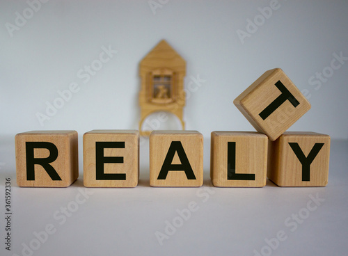 Cubes form the word 'realty' in front of a miniature house. Beautiful white background. Business concept.