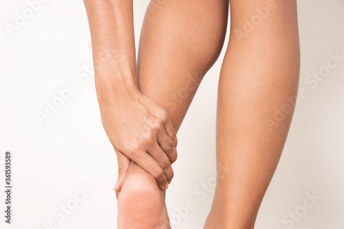 A young woman massaging her painful ankle with both hands , Isolated on white background