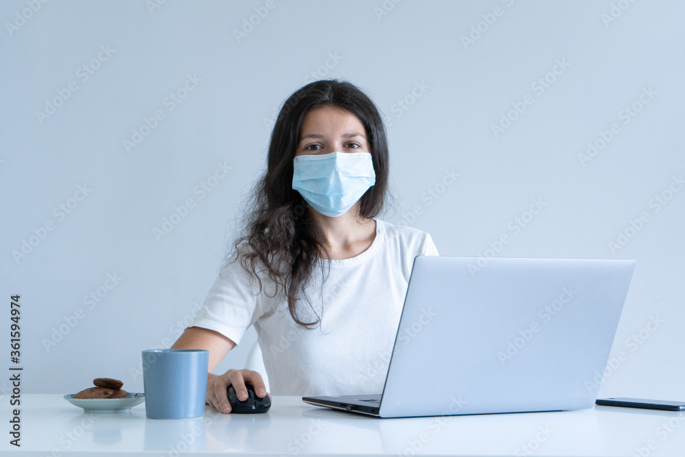 The girl works from home during quarantine. Corona virus pandemic. A girl in a surgical mask works on a laptop and drinks coffee. Distant work The girl works from home during quarantine. Corona virus pandemic. A girl in a surgical mask works on a laptop and drinks coffee. Distant work