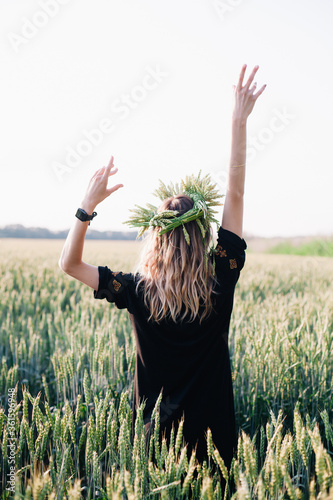 Young, slender girl in a wreath of wheat ears at sunset in a field