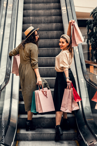 Two girls on an escalator in a shopping center. In the hands of paper bags. Shopping, leisure and entertainment.