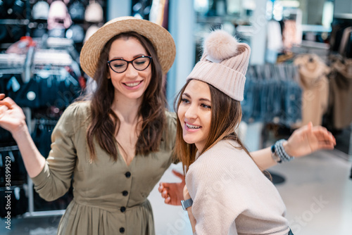 Trade, buyers. Two beautiful girls make purchases in a shopping center, go shopping. Funny fitting hats. The joy of consumption.