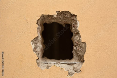 A hole cut in a yellow concrete wall for installing the elevator button.