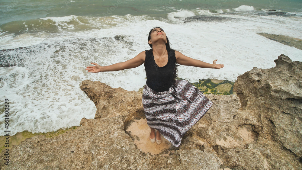 Φωτογραφία Indonesian girl enjoys life with outstretched hands on the rocky shore on the island of Bali