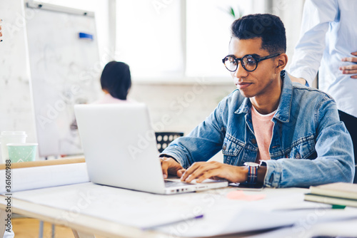 Skilled afro american male IT developer programming code for innovative application typing on laptop computer, casually dressed copywriter uploading multimedia files on website using wifi connection