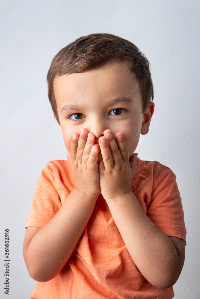 Cute three year old boy portrait, toddler covering his mouth with both hands. Cute three year old boy portrait, toddler covering his mouth with both hands.