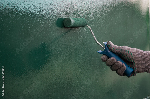 hand in a gray glove paints a wall in green