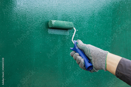 hand in a gray glove paints a wall in green