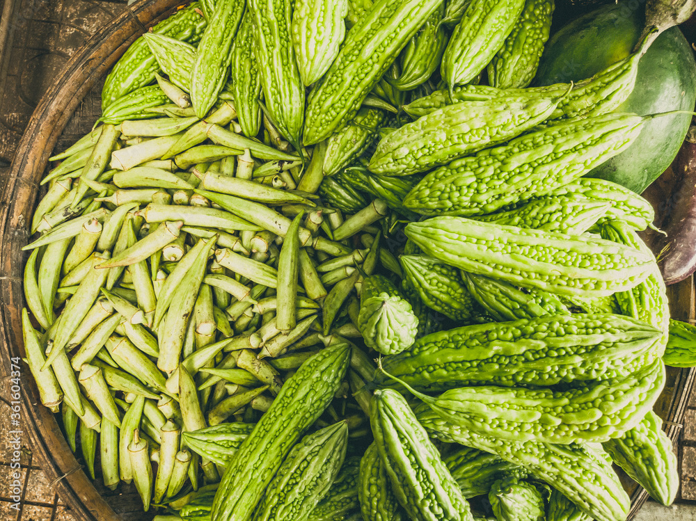 Closeup heap of momordica and okra in braided basket. Harvested young fresh organic bio antiparasitic, anthelmintic raw veggies on the market. Cooking, healthy food, vitamins for strong immunity Closeup heap of momordica and okra in braided basket. Harvested young fresh organic bio antiparasitic, anthelmintic raw veggies on the market. Cooking, healthy food, vitamins for strong immunity