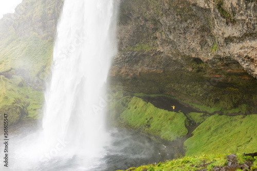 Tiny hiker behind the dramatic powerful waterfall in Iceland