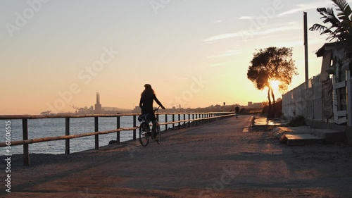 Silhouette of young curly girl riding a bicycle at the sunset on the promenade road to Barcelona, Catalonia, Spain. photo