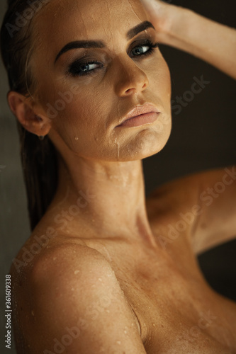 Relaxation and spa concept. Portrait of a sexy fashionable lady in a black swimsuit. Woman with wet hair and makeup poses in shower near swimming pool in natural light