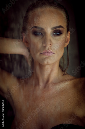 Relaxation and spa concept. Portrait of a sexy fashionable lady in a black swimsuit. Woman with wet hair and makeup poses in shower near swimming pool in natural light