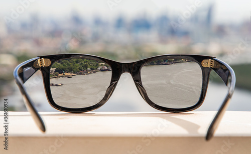 Bangkok, Thailand - Jun 09 2020 : Black eyeglass on a reflective surface. View through the lens of glasses that look at the Chao Phraya River.